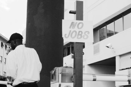 man in white dress shirt standing near white and black camera; Unemployment