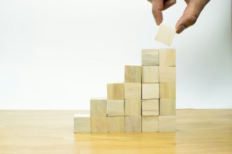 A person placing a piece of wood into a pyramid in their solo business.