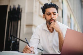 Adult man in white shirt working on a laptop outdoors, concentrating on his task.; new employer mindset