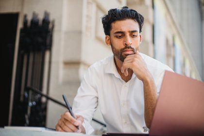 Adult man in white shirt working on a laptop outdoors, concentrating on his task.; new employer mindset