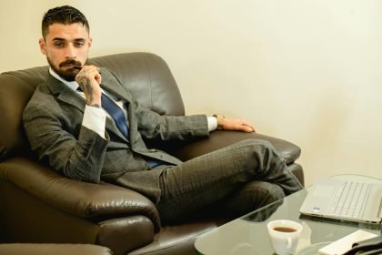 Pensive businessman in a suit sitting in an office chair with a laptop and coffee.; imposter syndrome for solopreneurs
