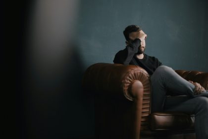 a man holds his head while sitting on a sofa; uncomfortable money conversations