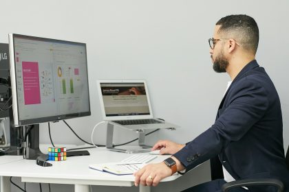 a man sitting at a desk with a laptop and a computer; business plateaus