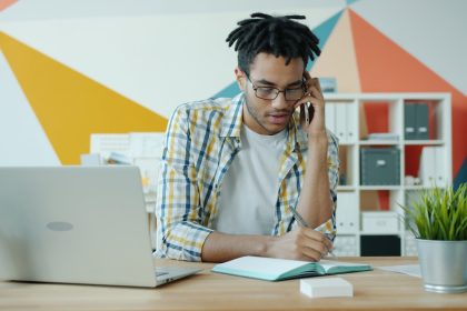 Man talking on phone at desk with laptop and notebook.; vetting business tools for freelancers