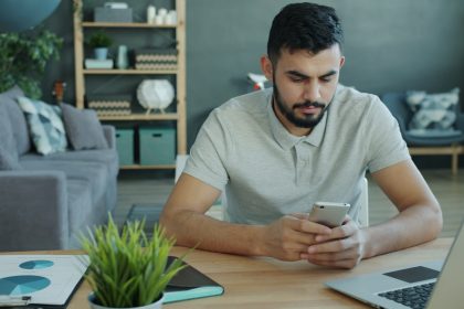 Man using smartphone at desk with laptop and charts.; feast famine cycles