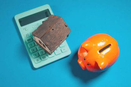 Calculator, piggy bank, and house model on blue background; auto-IRA for self-employed