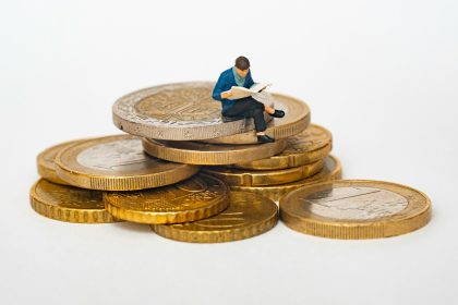 Miniature person sitting on stack of coins reading newspaper; freelance economy trends