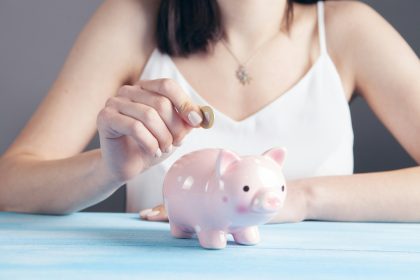 woman in white tank top holding pink pig figurine; solo 401k contribution limits