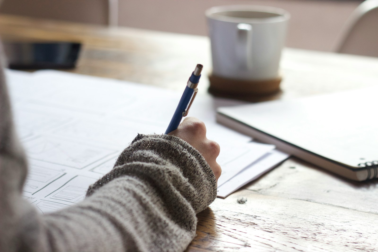 person writing on brown wooden table near white ceramic mug; Section 127 educational assistance