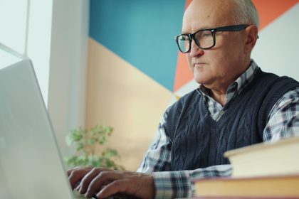 Elderly man with glasses using a laptop; seniors turning to gig work