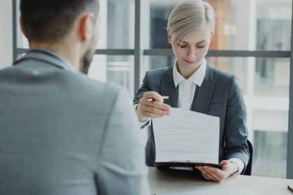 Woman in suit shows document to man; client onboarding checklist