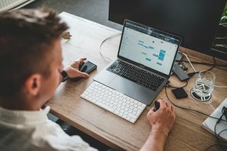 man holding mouse and iPhone while using Macbook Pro; do c corps get 1099