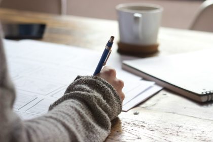 person writing on brown wooden table near white ceramic mug; how to become an seo freelancer