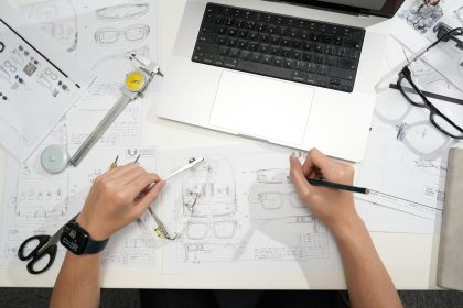 Designer sketching eyeglasses with laptop and tools.; accountable plan