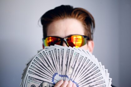 man in black framed sunglasses holding fan of white and gray striped cards; passive income ideas