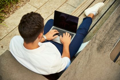 man wearing white sweatshirt using laptop computer sitting on sofa chair; 1099-sa