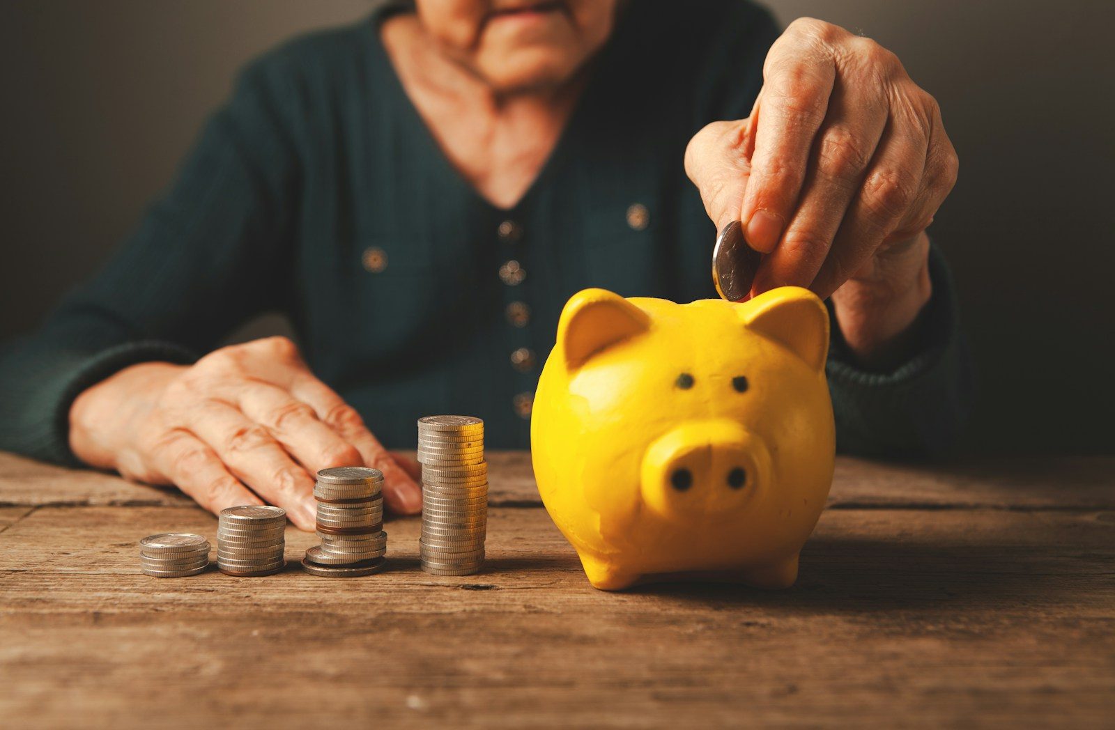 Elderly hands depositing coins into a yellow piggy bank; freelancer retirement savings