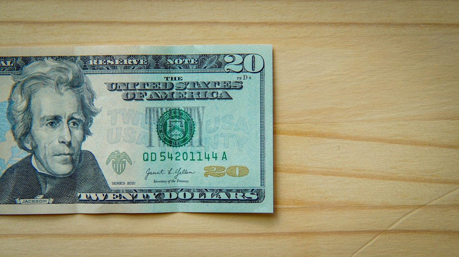 A twenty-dollar bill rests on a light wooden surface; July retail sales