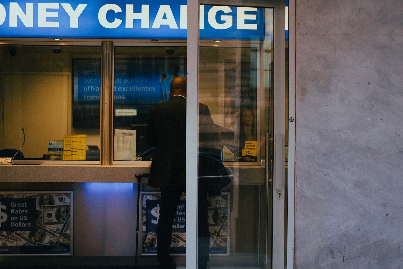 Man at a currency exchange office window, showing currency rates inside a bustling city; Fed rate hike small business