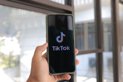 A hand holds a smartphone displaying the TikTok app in an indoor setting; TikTok One