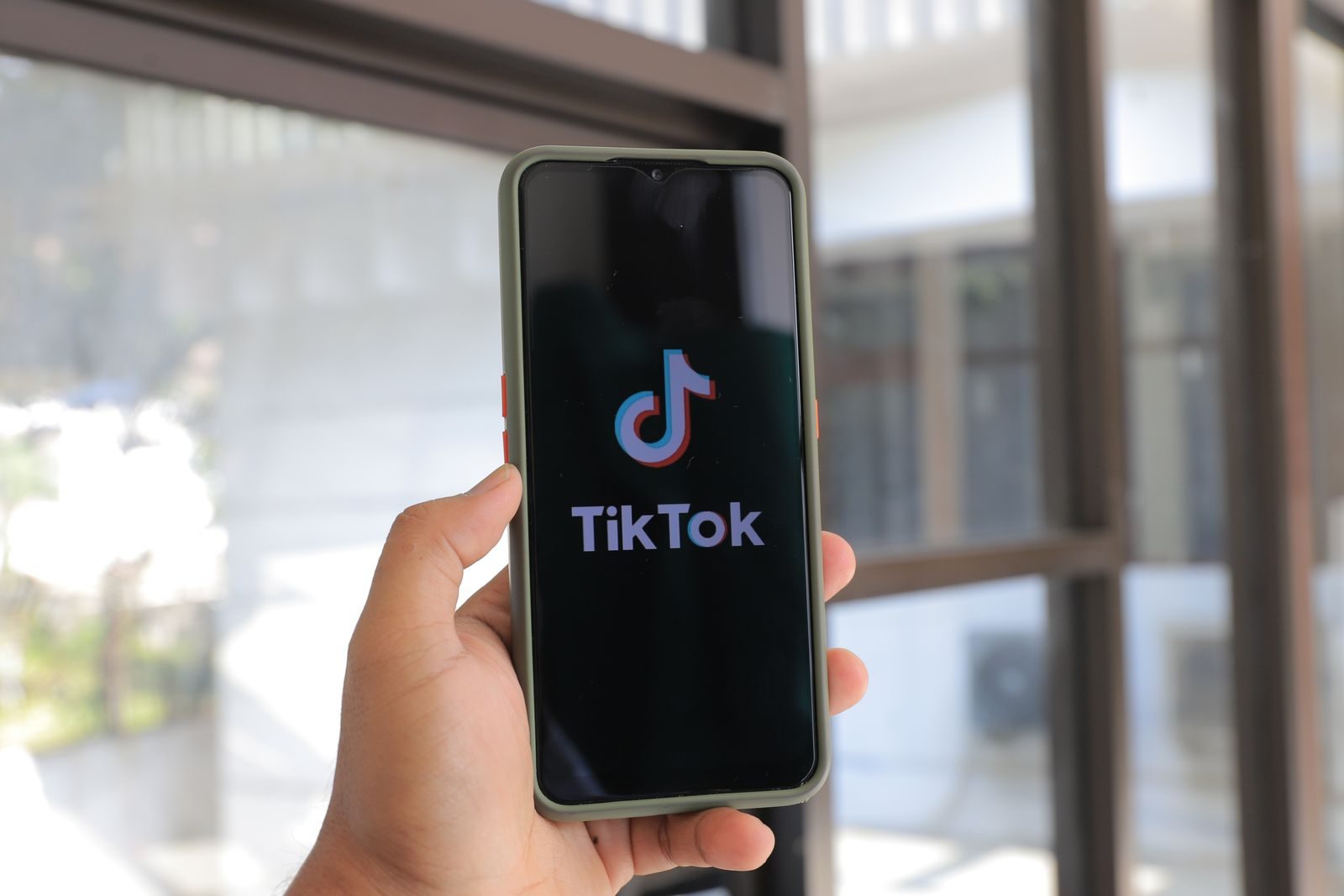A hand holds a smartphone displaying the TikTok app in an indoor setting; TikTok One