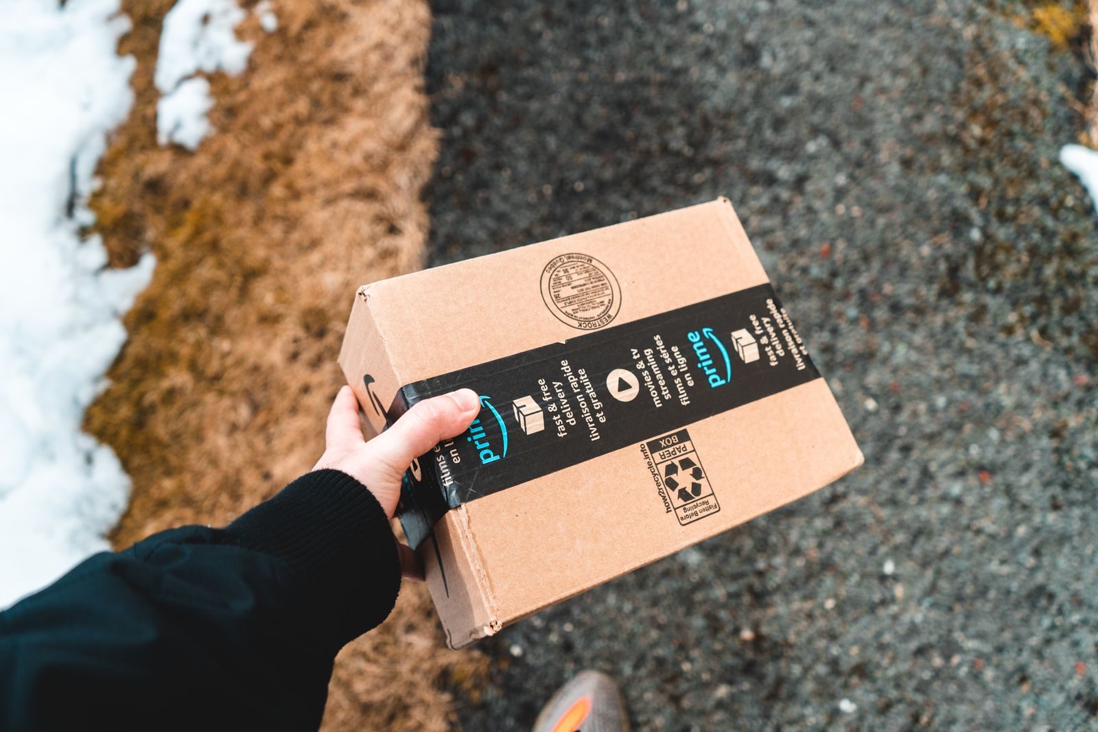 A person holding a cardboard Amazon Prime package on a snowy urban sidewalk; Amazon price history