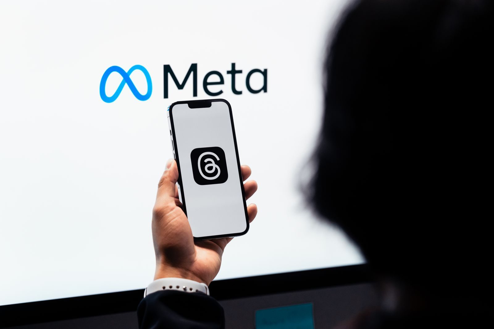 Hands holding smartphone with Meta Threads logo on screen, Meta branding in background; Meta One subscription