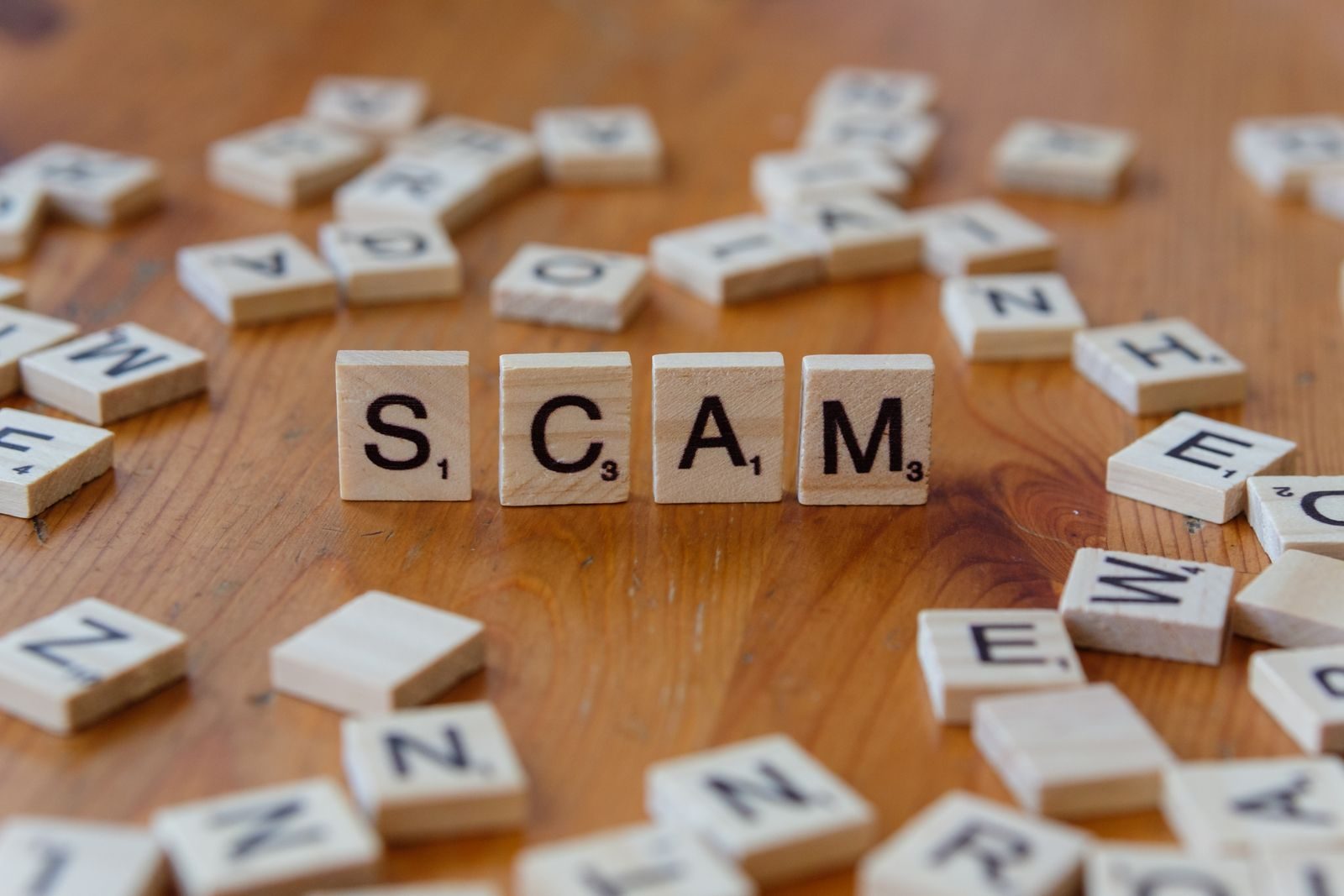 Image of Scrabble tiles spelling 'scam' surrounded by scattered letters on a wooden table; freelance job scams