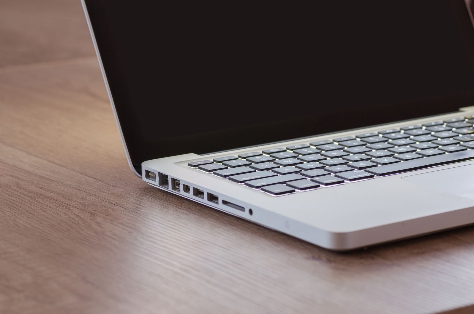 Close-up of a sleek silver laptop with a backlit keyboard on a wooden desk, perfect for tech themes; Constant Contact Claude connector