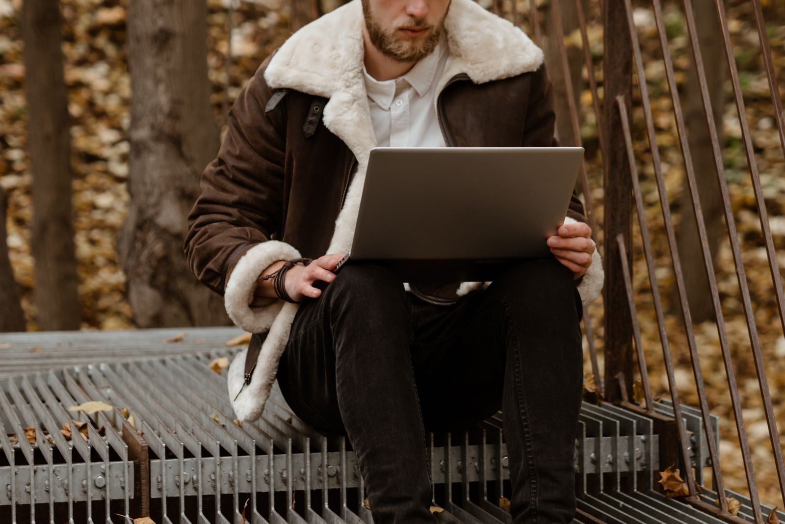 Stylish man working on laptop in an autumn park, embracing freelance lifestyle amidst natural scenery; fall hiring trends freelancers