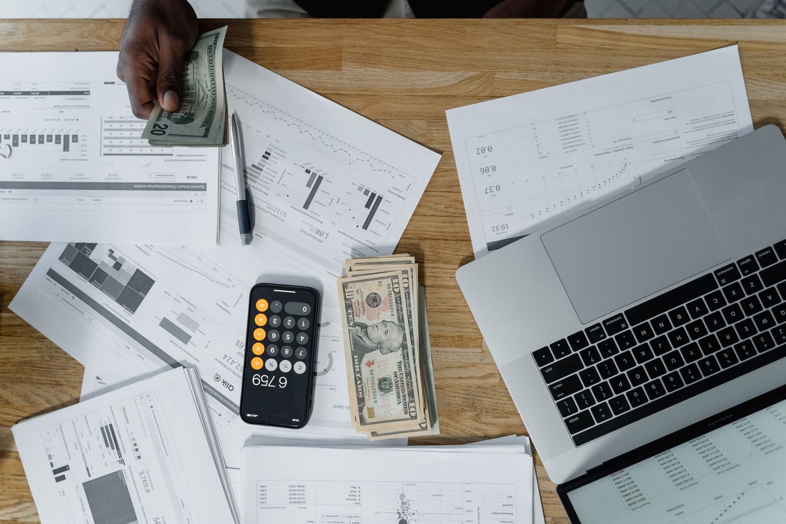 Overhead view of a busy workspace with cash, financial documents, and a laptop; AI-exposed jobs pay