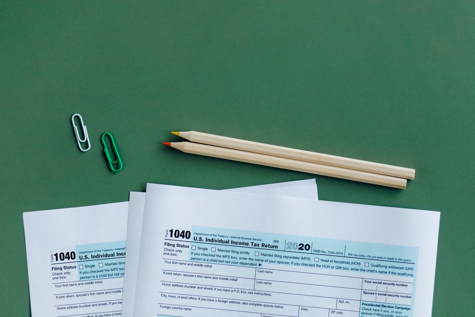 U.S. tax forms with pencils and paperclips on green surface in a flat lay setup; S corp partnership filing deadline
