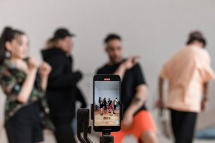 Group of dancers recording performance with smartphone on tripod, capturing trendy dance moves; creator communities