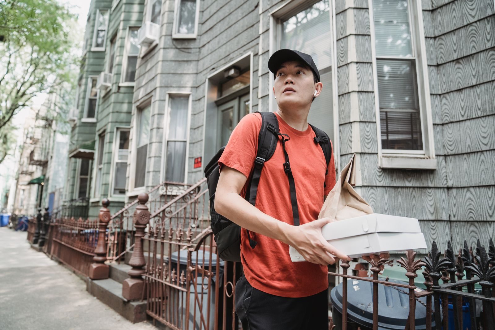 A delivery worker in a red shirt and cap holding packages outside a residential building; 2026 holiday seasonal hiring gig workers