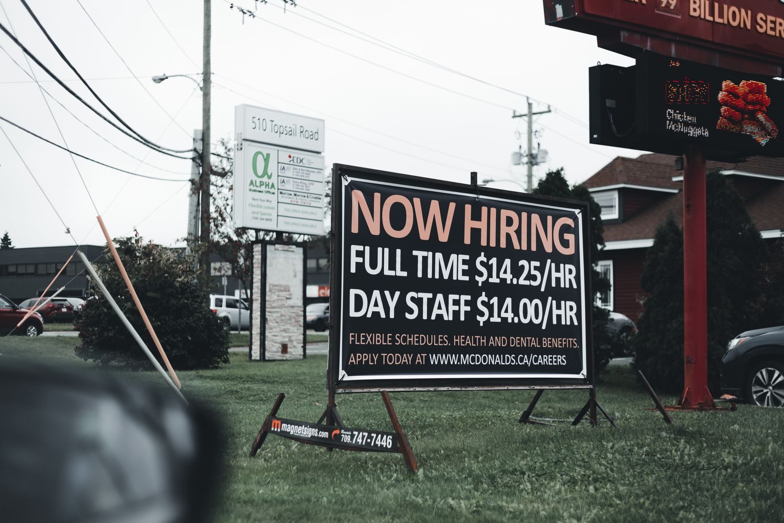 Outdoor hiring sign advertising restaurant job openings with competitive wages and benefits; jobless claims