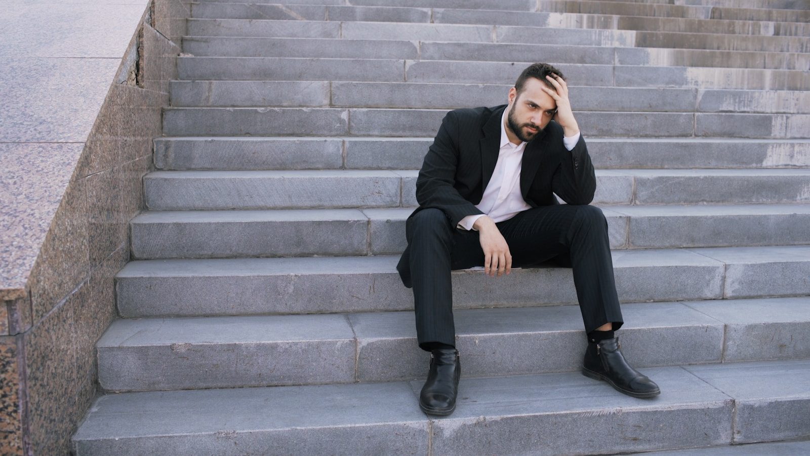 Man in suit sitting on outdoor stairs looking down; Challenger job cuts August 2026