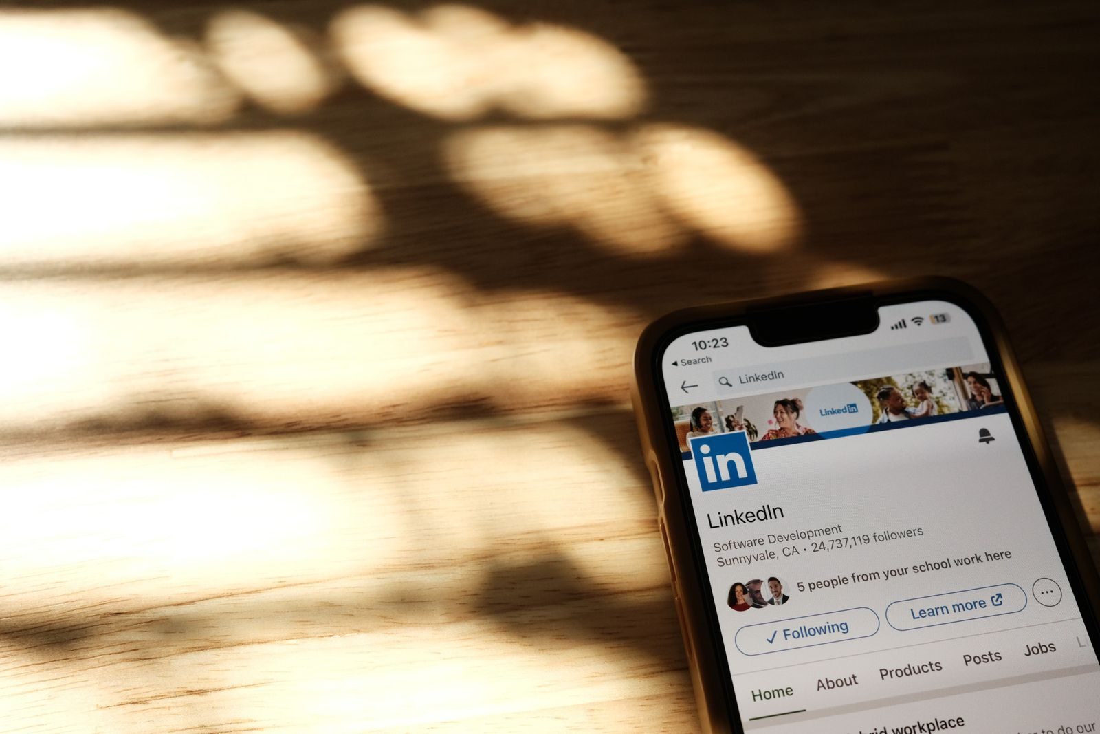 Close-up of a smartphone showing a LinkedIn profile page on a wooden table with shadows; LinkedIn creator monetization