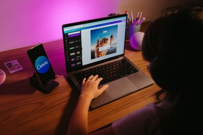 Teen working on graphic design using laptop at home with creative tools; Canva ProSuite