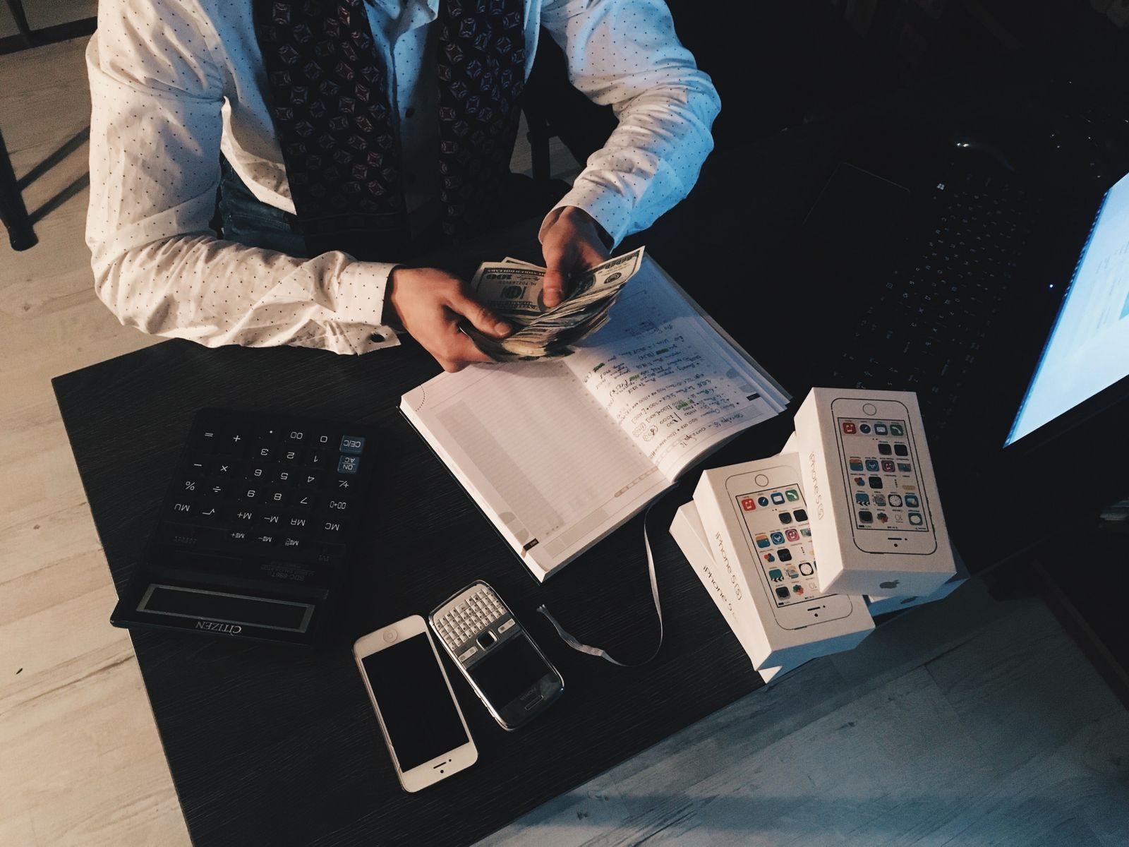 Businessman organizing finances with tech devices and cash on desk; AI bookkeeping