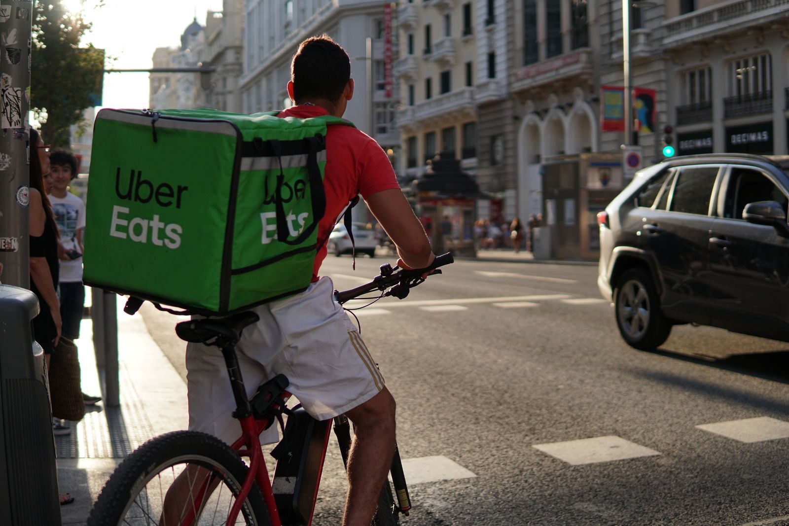 Delivery cyclist from Uber Eats riding through the bustling streets of Madrid; Uber ezCater acquisition