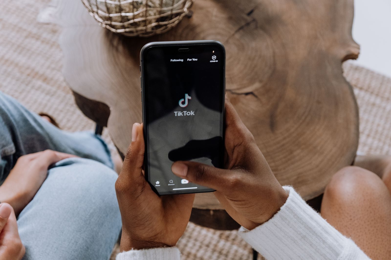 Close-up of hands holding a smartphone displaying the TikTok app interface on a wooden surface; TikTok Shop Black Friday