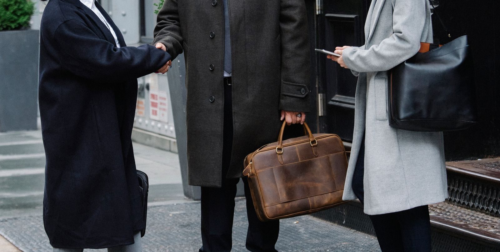 Crop anonymous trendy businessman and businesswomen in elegant outerwear shaking hands on street; WorkWhile settlement