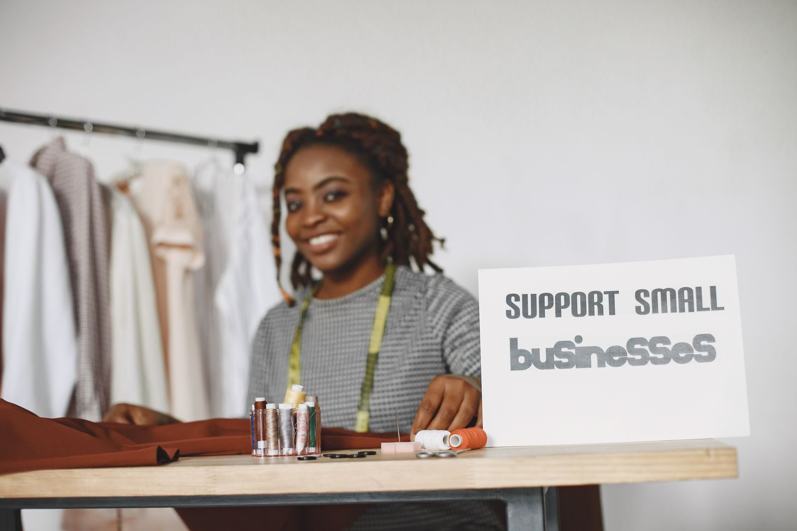 African American seamstress smiling at work with a 'Support Small Businesses' sign; Muse for Small Business