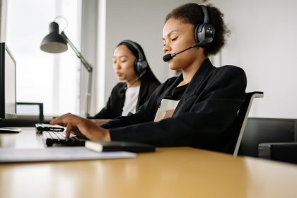 Two call center agents working at desks in an office setting with headsets; Gemini agent for work