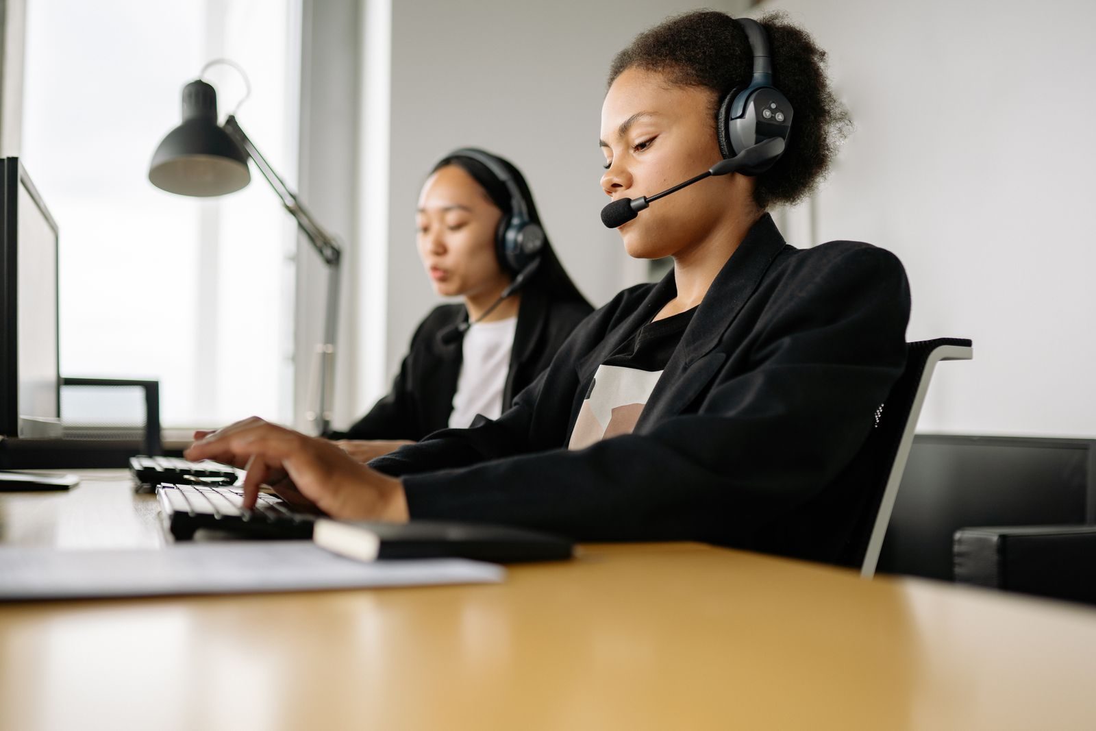 Two call center agents working at desks in an office setting with headsets; Gemini agent for work